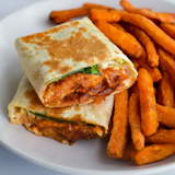 Two cut open wraps stacked on a white plate, filled with a spicy orange-red sauce and green lettuce, served next to sweet potato fries.